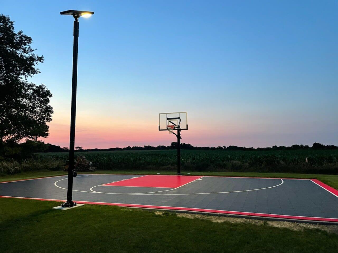 An outdoor basketball court with lights at dusk.