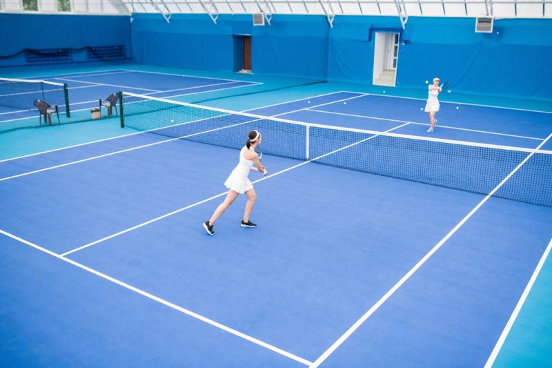 Two women playing tennis on a blue tennis court located at a Geo Site in Florida.